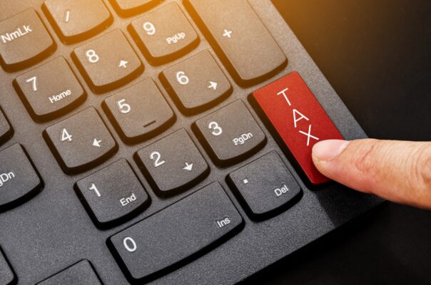A close-up image of a computer keyboard with a red key labeled "TAX" being pressed by a finger. The surrounding keys are black, and the finger is positioned over the red key, highlighting its significance.